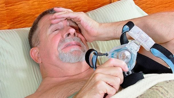 man in pain holding cpap mask