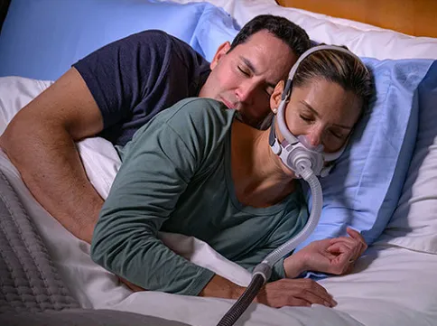 Man with CPAP mask laying in bed with woman. 