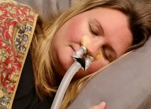 Woman lying in bed while wearing a nasal pillow CPAP mask.