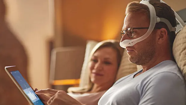 Man using CPAP mask while laying in bed. 