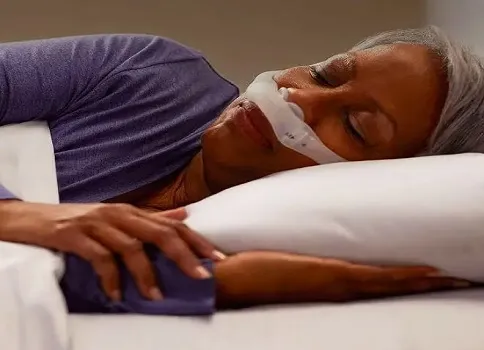 Woman lying in bed while wearing a nasal pillow CPAP mask.